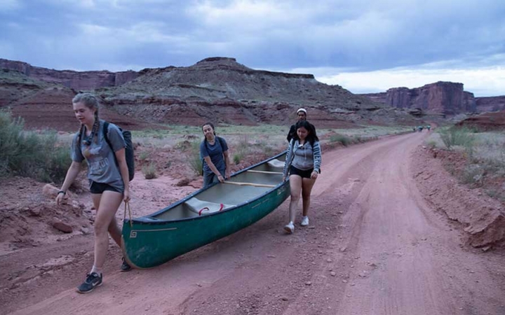 a group of three students carry a canoe on an outward bound trip in the southwest